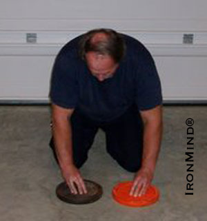 John Brookfield works on the Turn the Dial exercise using two barbell plates.  By working on the smooth surface of a garage floor the exercise is easier.  IronMind | Photo courtesy of John Brookfield.